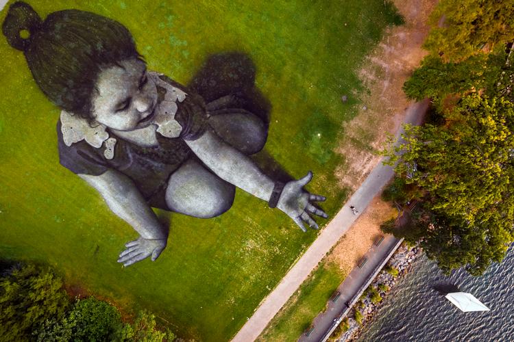 Landskabskunstværket her har titlen 'Message From Future'. Saypes værk dækker cirka 5.000 kvadratmeter, og den papirbåd, som pige netop har søsat i Genève-søen, repræsenterer ifølge kunstneren et budskab til verden om håb for fremtiden. Foto: Valentin Flauraud/Ritzau Scanpix