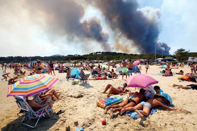 Strandgæster følger røgudviklingen fra en brændende bakke i Bormes-le-Mimosas i Frankrig. Foto: Jean-paul Pelissier/Ritzau Scanpix