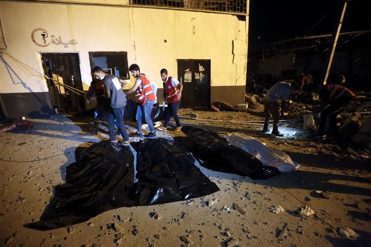 Hjælpearbejdere i fuld gang med arbejdet efter et luftangreb i en migrantlejr i Libyen. Forrest ser man plastikposer med lig i. 
Mindst 44 er dræbt i angrebet. Foto: Mahmud Turkia/Ritzau Scanpix