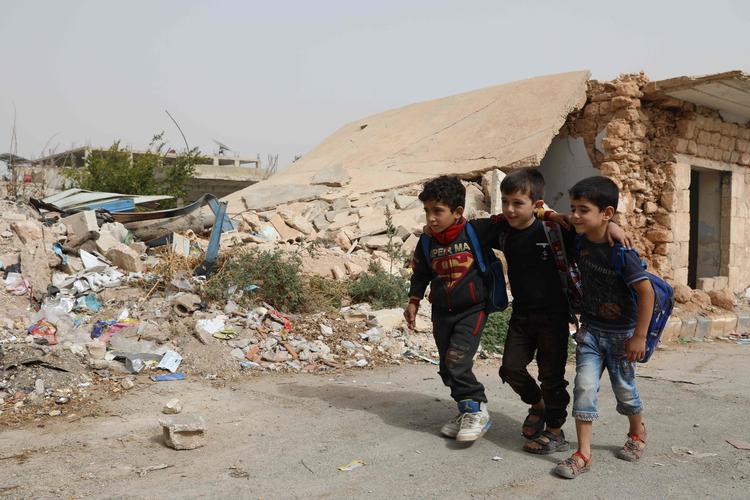 Tre skolebørn vandrer forbi en smaadret bygning i Binnish i Idlib-provinsen.  Foto: Omar Haj Kadour/Ritzau Scanpix