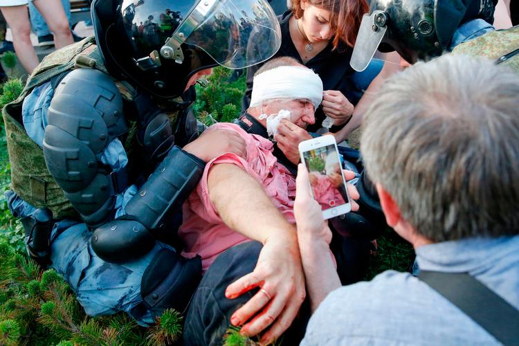 En demonstrant, der er kommet til skade under lørdagens demonstration i Moskva, hvor omkring 1.000 blev anholdt, og et medlem af Nationalgarden i kampudstyr Foto: Maxim Zmeyev/Ritzau Scanpix