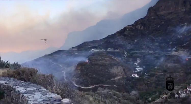 En helikopter kaster vand ned over en bjergside i Artenara på Gran Canaria. En kraftig skovbrand har siden lørdag raseret bjergene på øen. Situationen er endnu ikke under kontrol.  Foto: Carreteras Gc/Ritzau Scanpix