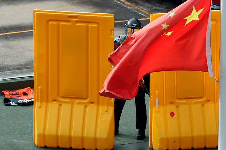 Det kinesiske flag blafrer i vinden foran en uro-betjent, der er sat ind for at bekæmpe demonstranterne i Hongkong.
   Foto: Tyrone Siu/Ritzau Scanpix