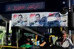 Syrere kører i bybus i hovedstaden Damaskus med billeder af Syriens præsident Bashar al-Assad i baggrunden.  Foto: Hassan Ammar/AP via Ritzau Scanpix