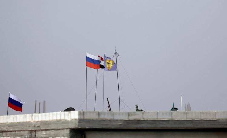 Russisk, syrisk og Manbij Military Councils flag blafrer sammen i vinden lidt uden for byen Manbij i Syrien. Manbij Military Council er en del af Syriens Demokratiske Styrker (SDF). Foto: Omar Sanadiki/Ritzau Scanpix