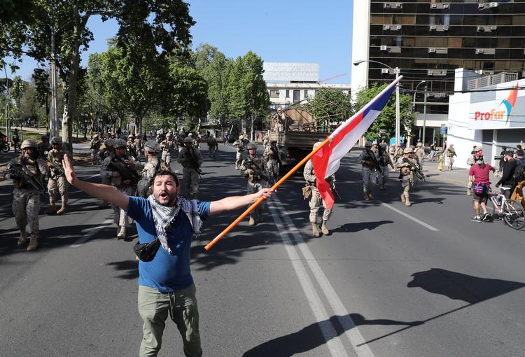 En demonstrant flager med det chilenske flag foran soldater.  

   Foto: Ivan Alvarado/Ritzau Scanpix