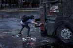 En demonstrant tager risikoen og går så tæt på, at den ikke kan ramme ham, mens han laver grafitti på en af politiet vandkanoner i Santiago, Chile.  Foto: Mads Nissen/POLFOTO