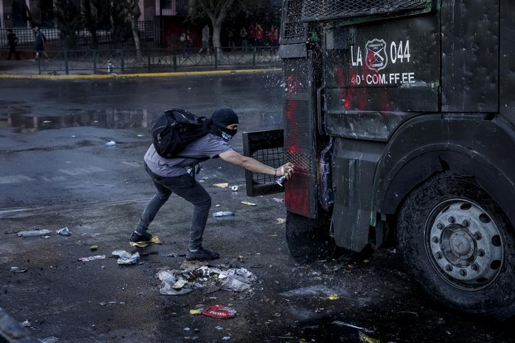 En demonstrant tager risikoen og går så tæt på, at den ikke kan ramme ham, mens han laver grafitti på en af politiet vandkanoner i Santiago, Chile.  Foto: Mads Nissen/POLFOTO