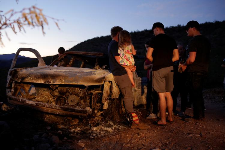 Pårørende til de afdøde står ved gerningsstedet på en landevej i det nordlige Mexico. Fem af i alt ni ofre døde ved, at bilen på billedet sprang i luften. Foto: Jose Luis Gonzalez/Ritzau Scanpix