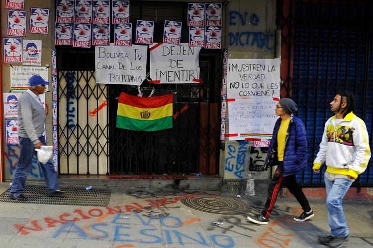 Bolivianere går forbi indgangen til den statsejede tv station , hvor demonstranter har hængt budskaber op om præsident, Evo Morales. Foto: Jorge Bernal/Ritzau Scanpix