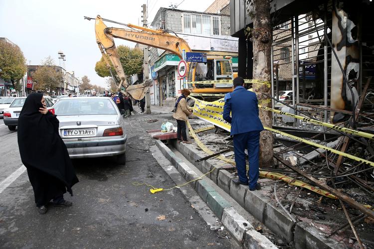 
    En kvinde ser til, mens demonstranter hænger et banner op på en afsvedet bank i Irans hovedstad, Teheran. Ifølge menneskeretsgruppen Center for Human Rights in Iran, er mellem 180 og 450 personer dræbt i løbet af fire dage med intens vold, efter at prisstigningerne på benzin blev offentliggjort 15. november Foto: Wana News Agency/Ritzau Scanpix