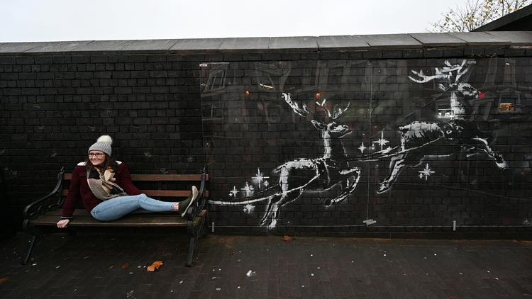 Der har været usædvanligt travlt foran en ellers uanselig bænk i Birmingham, efter Banksy prægede væggen ved siden af den med to hvide rensdyr i sidste uge.  Foto: Paul Ellis/Ritzau Scanpix