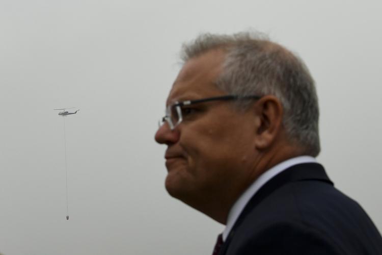 En helikopter, der flyver ud for at slukke skovbrande, ses bag Australiens premierminister Scott Morrison på billedet taget 5. januar. Foto: Stringer/Ritzau Scanpix