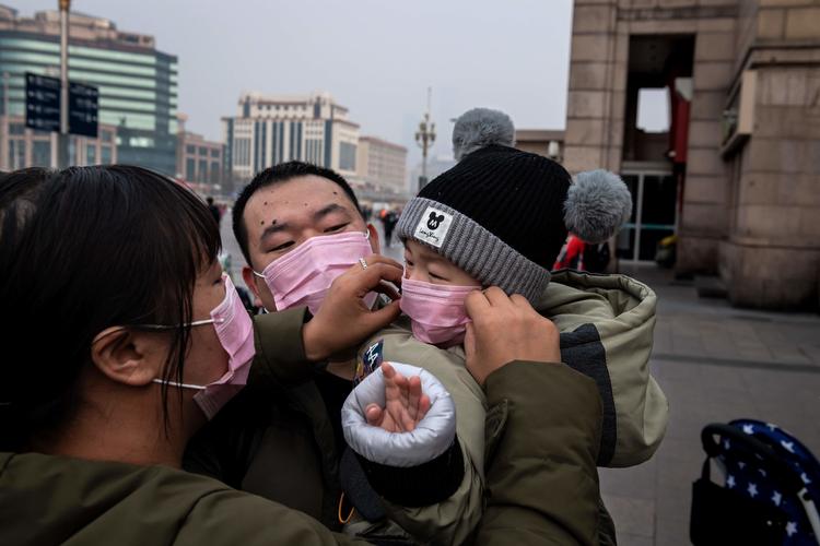 Et forældrepar fra Wuhan hjælper deres lille barn med at få en maske på. Foto: Nicolas Asfouri/Ritzau Scanpix