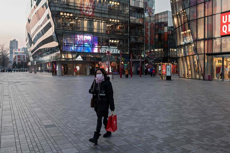 En kvinde iført beskyttelsesmaske går foran et mennesketomt indkøbscenter i Beijing.  Foto: Nicolas Asfouri/Ritzau Scanpix