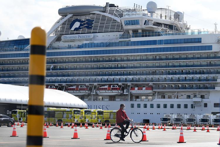 En mand cykler forbi busser, der venter på at transportere de første passagerer fra skibet Diamond Princess i Yokohama, Japan. Passagererne på skibet har været i karantæne i to uger. 540 var smittet med coronavirus.  Foto: Charly Triballeau/Ritzau Scanpix