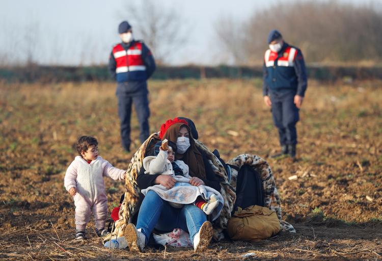 Migranter hviler sig ved Pazarkule, en af Tyrkiets grænser til Grækenland, med tyrkiske gendarmere bag dem.  Foto: Leonhard Foeger/Ritzau Scanpix