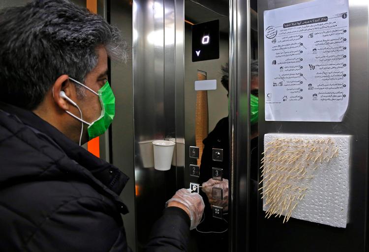 En mand i Iran bruger en tandstikker til at trykke på en knap i en elevator for at undgå at blive smittet og sprede smitte af coronavirus. Foto: Atta Kenare/Ritzau Scanpix