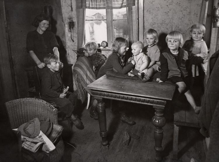 Her ses en mor med sine syv børn i et typisk arbejderhjem i slutningen af 1920'erne. Her måtte man tilsyneladende godt have fødderne på bordet. Foto: Arbejdermuseet