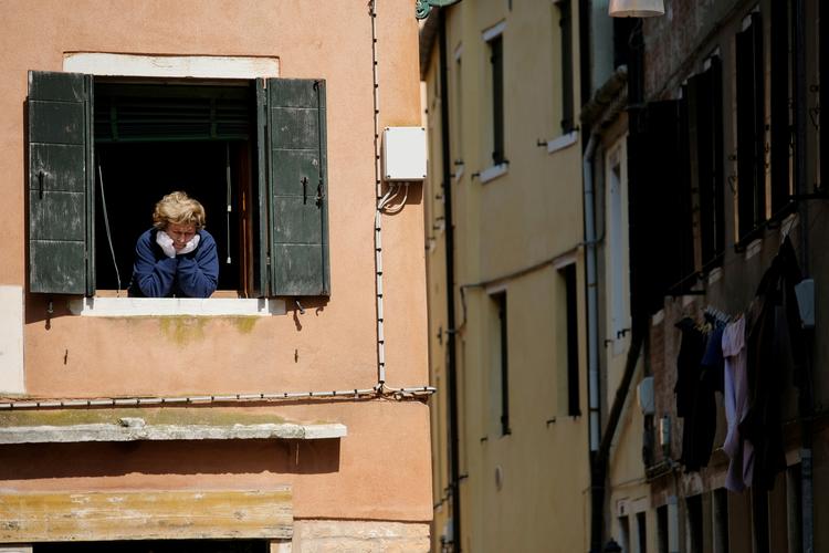 En kvinde følger livets gang udenfor vinduet fra sin lejlighed i Venedig. Nu kan hun og alle andre italienere se frem til en langsom åbning af landet.       Foto: Manuel Silvestri/Ritzau Scanpix