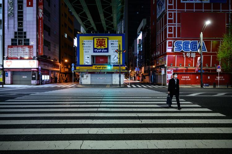 En med mand krydser gaden i området Akihabara i Tokyo. Landets sundhedsvæsen er så presset, at akutafdelinger er begyndt at afvise patienter. Foto: Philip Fong/Ritzau Scanpix