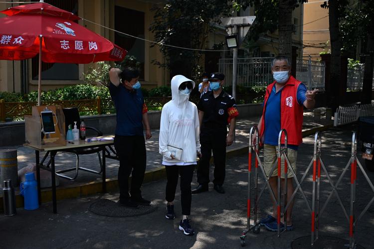 En kvinde, der bærer mundbind, passerer en sikkerhedsvagt, der tjekker folks temperatur ved indgangen til et beboelsesområde i Beijing. Byen har haft en opblussen af coronavirus. Forskere mener, det er medbragt fra Europa.  Foto: Wang Zhao/Ritzau Scanpix