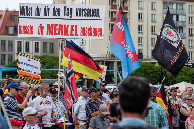 Pegida-demonstrationens største bifald kommer, da en taler meddeler, at ingen migranter lige nu reddes fra at drukne i Middelhavet. På det store skilt står der noget i stil med: »Hvis du vil spolere din dag, behøver du bare kaste et blik på Merkel«. Det er kansler Angela Merkel, der tænkes på. 
 Foto: Stringer/Ritzau Scanpix