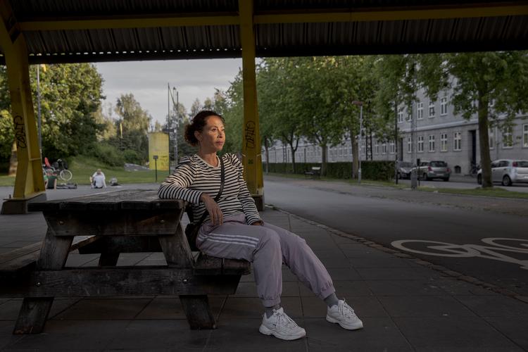 Lokal beboer Charlotte Urne under det metaltag, der på en hed sommeraften er med til at samle og forstærke lyden fra Soundbokse fra det grønne anlæg ved Nørrebroparken.  Det lille sorte skilt, der maner til ro efter kl. 22, kan anes bag hendes skulder op ad den gule bygning. Foto: Peter Hove Olesen/POLFOTO
