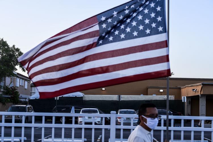  En 54-årig mand, Oscar Marquez, går med det amerikanske flag foran et begravelseshjem, hvor en container til de døde er opstillet, i Hialeah nær Miami. Florida er en af de stater, der har mange smittede og døde af covid-19.  Foto: Chandan Khanna/Ritzau Scanpix