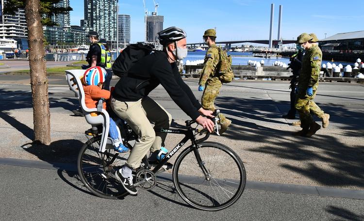 En cyklist passerer soldater i Melbourne. Storbyen indfører udgangsforbud, der skal gælde om aftenen og natten de næste seks uger. Det sker, fordi antallet af smittede med covid-19 er stigende.   Foto: William West/Ritzau Scanpix