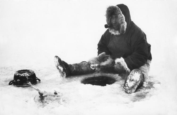 Man mener, at ordet eskimo etymologisk set betyder 'den der spiser råt kød'.  Her er det en grønlandsk fanger, der venter på fisk, mens han nyder en pibe tobak.  Foto: Polfoto/POLFOTO