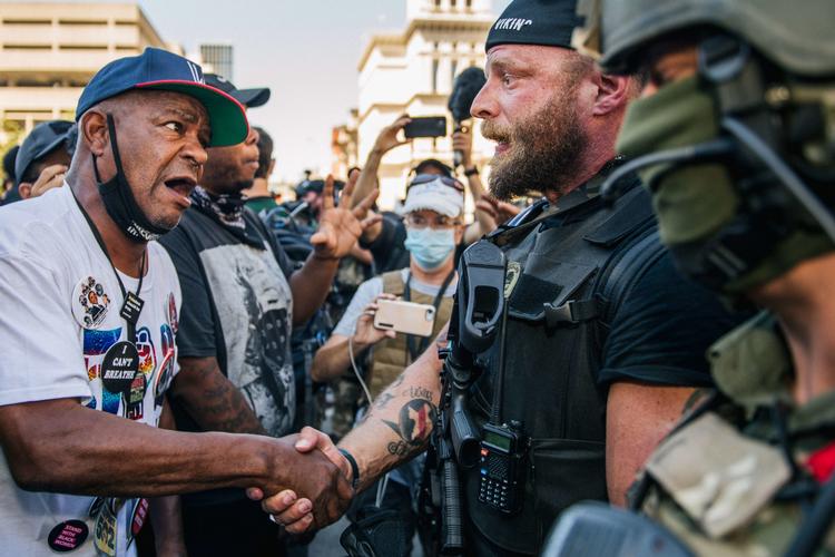 En højreorienteret trykker hånd med en Black Lives Matter-demonstrant i Louisville, Kentucky. Selv om der har været voldsomme optøjer, er mere end 93 procent af BLM-demonstrationer i USA er foregået uden alvorlige skader, viser ny rapport. Foto: Brandon Bell/Ritzau Scanpix