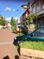 I denne gågade i tyske Bad Seegeberg har de handlende placeret vidt forskellige kummetyper foran deres butikker, som skal illustrere, hvad de handler med. Så her må vi formode, at der er tale om en butik, der handler med noget bilrelateret. Bemærk også vandkanderne, der er hængt op over gaden. Foto: Anette Meilandt. 