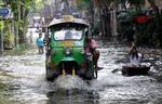 En tuk-tuk overhaler en kvinde i en robåd i et oversvømmet Bangkok.  Foto: Sakchai Lalit/Ritzau Scanpix