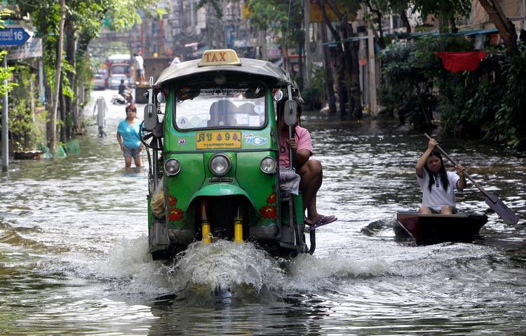 En tuk-tuk overhaler en kvinde i en robåd i et oversvømmet Bangkok.  Foto: Sakchai Lalit/Ritzau Scanpix