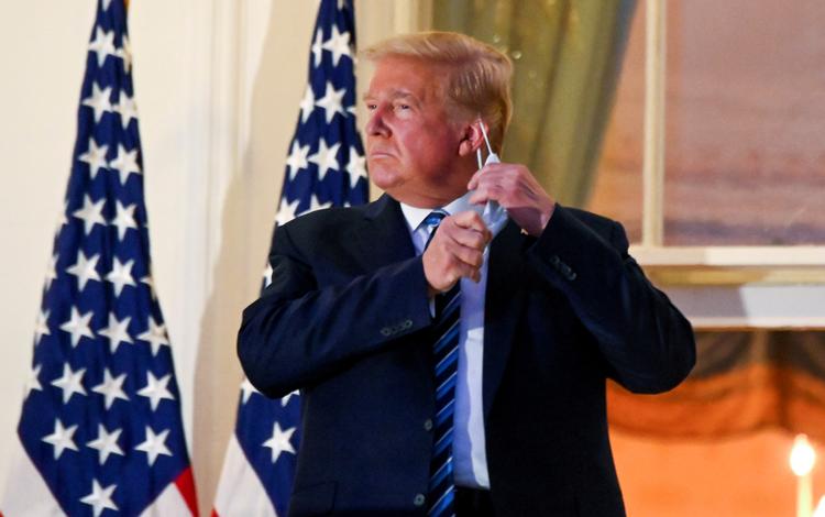 Præsident Donald Trump tager sit mundbind af på en balkon i Det Hvide Hus efter at være blevet udskrevet fra hospitalet mandag.  Foto: Erin Scott/Ritzau Scanpix