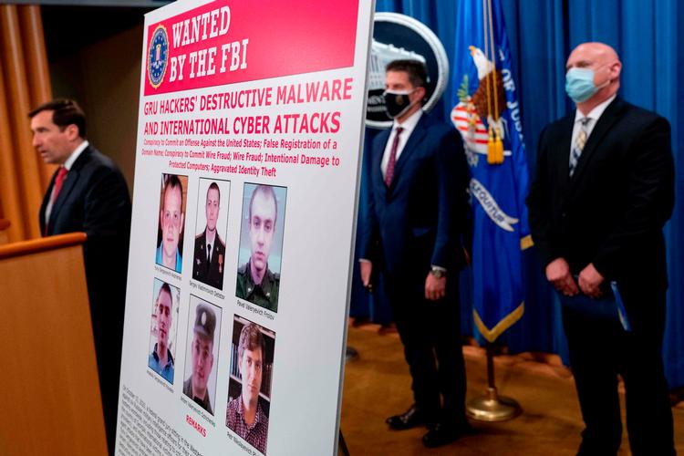 En plakat med de seks personer, der er eftersøgt for cyberangreb, blev præsenteret på et pressemøde.  Foto: Andrew Harnik/Ritzau Scanpix
