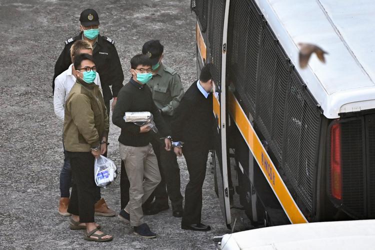Demokratiforkæmperen Joshua Wong (i midten) blev sammen med en anden aktivist, Ivan Lam (tv.), iført håndjern ført ind i en politibus, der onsdag førte dem til den retsbygning, hvor de fik deres dom. Foto: Anthony Wallace/Ritzau Scanpix
