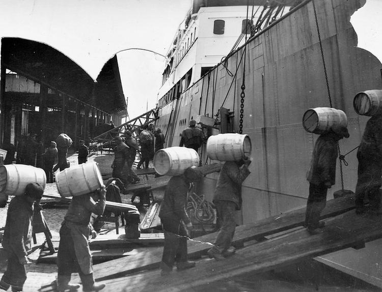Smørdritler på godt 50 kilo bæres ombord på Englandsbåden. I baggrunden ses de halve flæskekroppe, som også blev eksporteret tili briterne. 