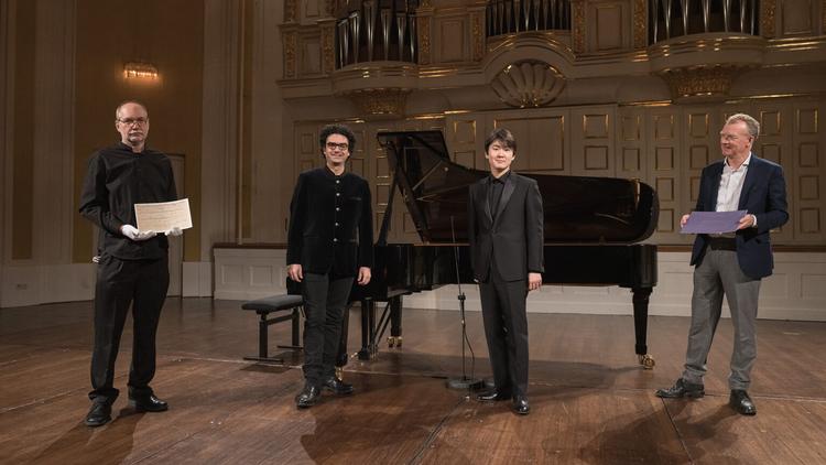 Den kunstneriske leder af Mozart-festugen i Salzburg, Rolando Villazón, og pianisten Seong-Jin Cho omgivet af folk, der viser manuskriptet til det lille klaverstykke af Mozart frem. Foto: PR-foto