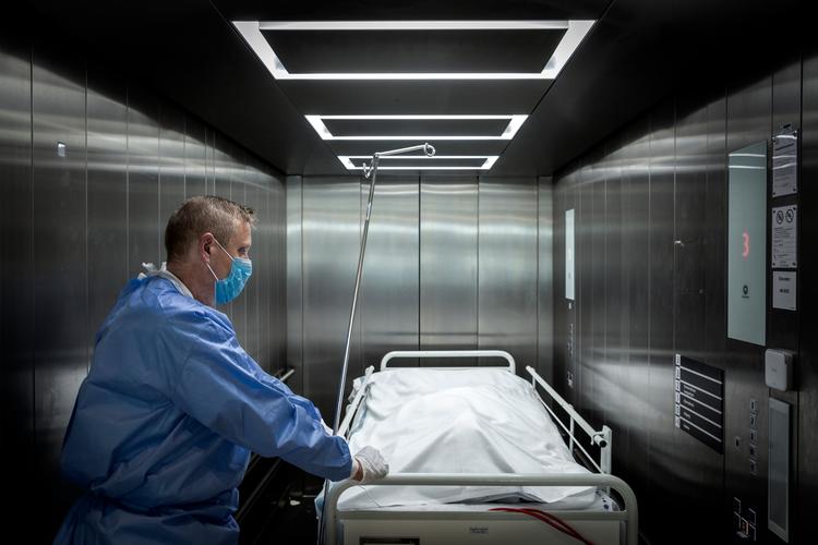 En ældre patient er død af følgevirkningerne af coronavirus på Slagelse Sygehus, og portør Jan Petersen kører den afdøde væk fra stuen.  Foto: Mads Nissen/POLFOTO