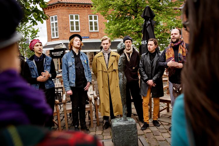 Mens Holstebro i årtier har forskønnet sig med kunstværker som Alberto Giacomettis berømte 'Kvinde på kærre', har København været for dårlig til at sikre ny kunst på veje og pladser, erkender socialdemokraterne i hovedstaden.
Her synger en teatertrup fra Polen for Giacomettis skulptur foran det gamle rådhus under festugen i byen i 2017. Foto: Astrid Dalum/POLFOTO
