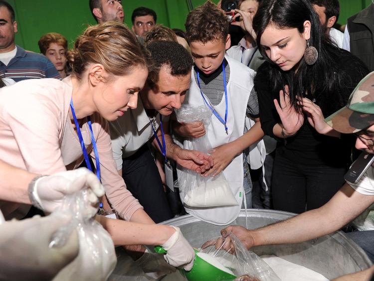Syriens præsident Bashar al-Assad (nr. 2 fra venstre) og hans kone, Asma (tv.), uddeler nødhjælp til sultne indbyggere i Damaskus. rollen som den alfaderlige landsleder dyrker Assad på Instagram, mens virkeligheden er en ganske anden. Foto: Sana/Ritzau Scanpix