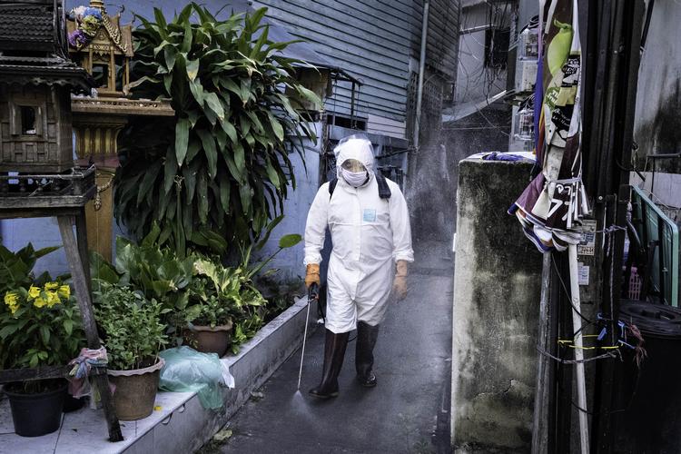 En mand iført sikkerhedsdragt sprøjter desinficerende væske ud på alle flader ved et hus i Bangkok, hvor en hel familie er blevet smittet med corona. Foto Claus Blok Thomsen