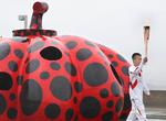 Yayoi Kusama er en af Japans meget karakteristiske kunstnere, kendt for sine prikker, ikke mindst de prikkede græskar. Her bæres den olympiske fakkel forbi et af dem i  Naoshima i det vestlige Japan.    Foto: Uncredited/Ritzau Scanpix