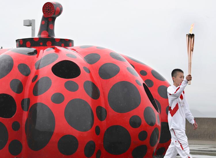 Yayoi Kusama er en af Japans meget karakteristiske kunstnere, kendt for sine prikker, ikke mindst de prikkede græskar. Her bæres den olympiske fakkel forbi et af dem i  Naoshima i det vestlige Japan.    Foto: Uncredited/Ritzau Scanpix