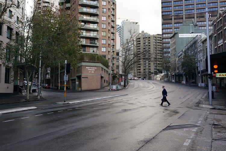 En fodgænger krydser en stille gade i Sydney. 18 millioner australiere, svarende til 70 procent af befolkningen, er nu underlagt en eller anden form for coronarestriktioner. Foto: Loren Elliott/Ritzau Scanpix
