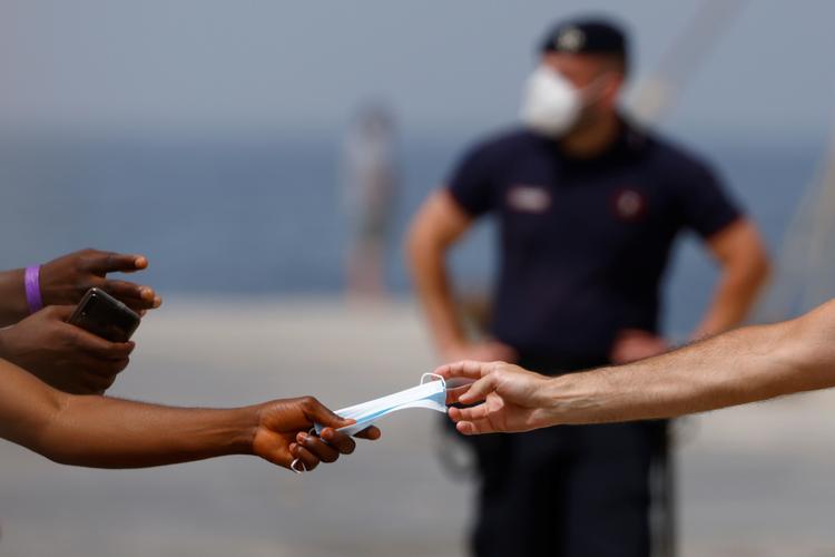 Migranter kommer til Europa via flere veje. Her giver politiet på den italienske ø Lampedusa et mundbind til en migrant, der er kommet til øen og som skal videre til fastlandet. Den danske ambition om et modtagecenter i et afrikansk land lever endnu. Udenrigsminister Jeppe Kofod besøger tirsdag og onsdag Marokko, der bringes i spil til at huse modtagecenter. Foto: Guglielmo Mangiapane/Ritzau Scanpix