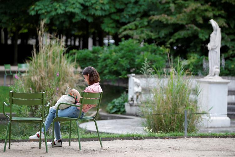 En kvinde har slået sig ned med en bog Tuilerierne i Paris. Selv om Frankrig har dalende smittetal, vinder den smitsomme Delta-variant frem.  Foto: Sarah Meyssonnier/Ritzau Scanpix