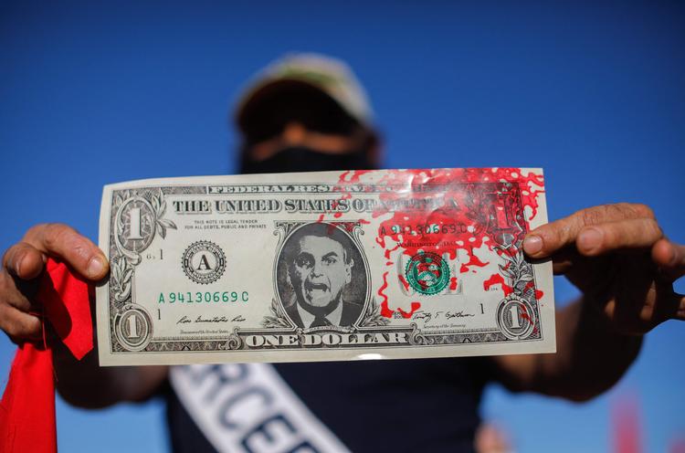 En mand holder en blodig dollar-seddel med billedet af den brasilianske præsident, Jair Bolsonaro. Manden deltog i demonstrationen i Brasilia mod Bolsonaros håndtering af coronakrisen.  Foto: Sergio Lima/Ritzau Scanpix